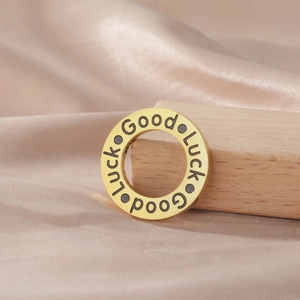 Close-up of golden stainless steel ring pendant with Good Luck engraving on satin cloth