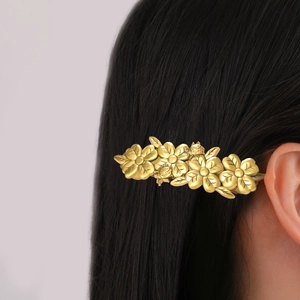 Elegant gold flower hair clip with five petals and leaves on smooth black hair