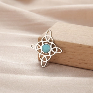 Detalle del colgante de nudo de bruja plateado con piedra azul sobre tela de seda