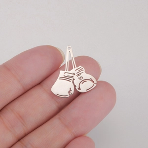 Détail macro de pendentifs gants de boxe en acier doré 18 carats tenus entre les doigts