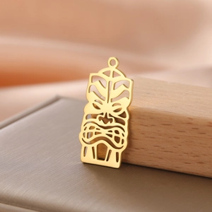 Detailed view of hollowed 18K gold-plated Tiki mask pendant with polished steel finish