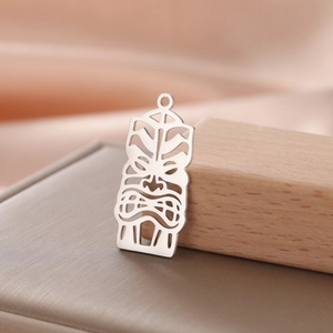 Macro shot of silver cutout Tiki totem pendant displayed on wood and leather textures