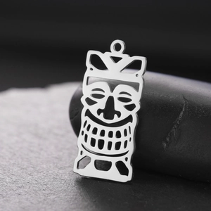 Macro view of a silver stainless steel hollow Tiki mask pendant on a black stone