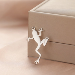 Polished stainless steel frog pendant charm for necklaces on a jewelry box edge