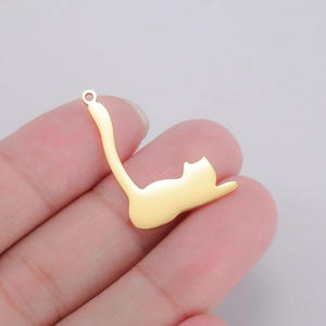 Polished gold kitten charm pendant held against fingers to show the actual size scale