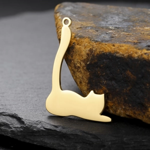 Macro detail of a mirror-polished golden cat-shaped pendant on a textured stone surface
