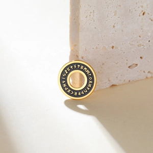 Detail of gold and black rune pendant resting on stone showing intricate Norse engraving