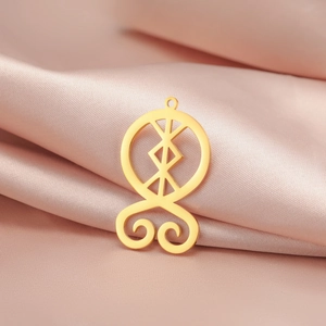 Detailed view of a gold cutout geometric rune pendant on soft pink satin fabric