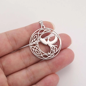 Detailed close-up of a hollow silver phoenix pendant with Celtic knot patterns on a hand