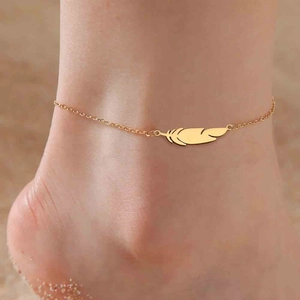 Detalle de un colgante de pluma en oro de 18K en una tobillera usada en la playa