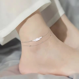 Detalle de la tobillera de doble capa de acero con colgante de pluma y cuentas en modelo