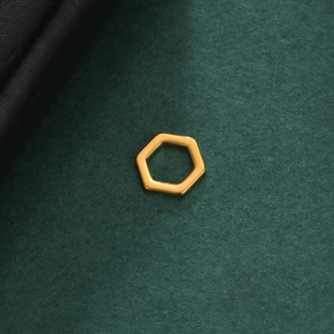 Macro detail of a polished gold-plated hollow hexagonal pendant on a textured dark background