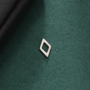 Macro view of minimalist silver rhombus earring on premium textured dark green background