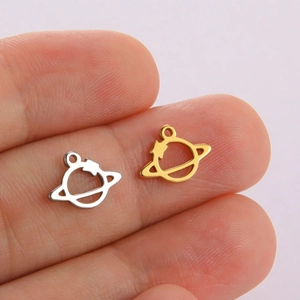 Macro shot of tiny gold and silver planet-shaped stainless steel charms held on fingertips