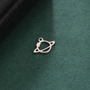 Macro shot of a silver planet charm with a Saturn-like ring on textured green paper