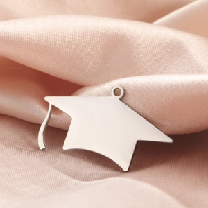 Close-up of silver graduation cap charm with tassel on pink satin fabric background