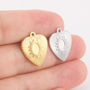 Pendentifs en cœur avec motifs soleil en acier doré et argenté tenus à la main