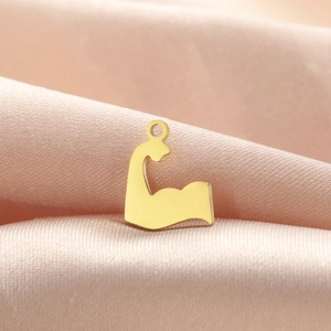 Detailed macro view of gold-plated muscular arm pendant on soft peach satin fabric