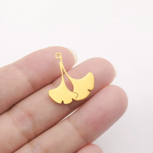 Close-up of golden ginkgo leaf charm showing size held by hand for DIY jewelry making