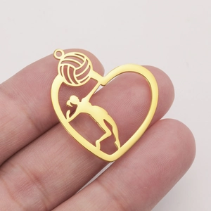 Golden heart pendant with hollow volleyball player design held by hand for scale