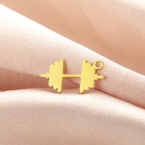 Close-up of golden dumbbell pendant on pink silk, showing polished metal texture