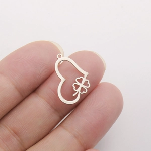 Macro detail of a stainless steel heart and four-leaf clover pendant held between fingers.