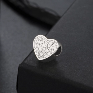 Vue macro d'un pendentif cœur en acier inoxydable avec gravure NANA et détails floraux