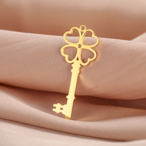 Détail d'un pendentif clé trèfle à cœurs en or poli sur un tissu en soie de couleur champagne
