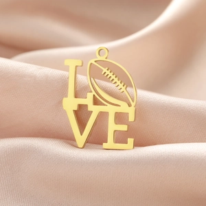 Dettaglio macro del ciondolo LOVE dorato con design palla da rugby su sfondo seta