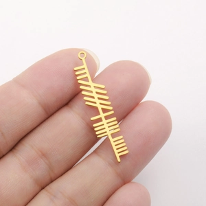 Close-up of golden stainless steel Celtic Ogham bar pendant shown on fingertip for scale