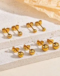 Detailed view of four pairs of golden stainless steel ball earrings on stone