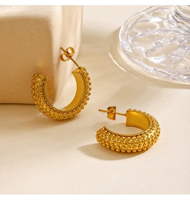 Detailed close-up of C-shaped golden earrings with textured beaded surface on stone
