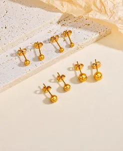 Close-up of golden ball stud earrings in various sizes on a textured travertine stone