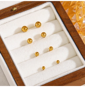 Detail showing four sizes of polished gold ball stud earrings arranged in a wooden box