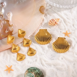 Gouden schelp oorbellen en speld set op wit zand met decoratieve zee-elementen
