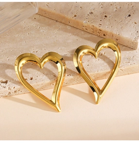 Detailed view of oversized polished gold heart earrings on a natural stone background