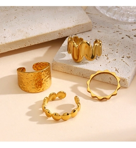 Detalle de cuatro anillos minimalistas dorados con texturas martilladas y perladas en piedra