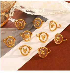 Dettaglio di anelli a lettera vintage in oro con cornice ovale su sfondo di pizzo bianco