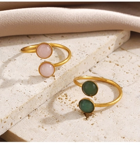 Detalle de anillos bañados en oro de 18k con piedras rosas y verdes sobre fondo de piedra