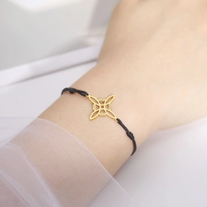 Detail van de 18K gouden heksenknoop hanger aan een zwart verstelbaar geweven armbandje