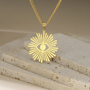 Golden stainless steel necklace with sunburst eye pendant on cream stone background