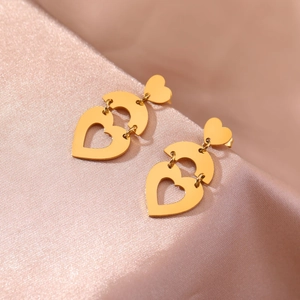 Dreistufige goldene hohle Herz-Ohrhänger elegant präsentiert auf rosa Seidenstoff