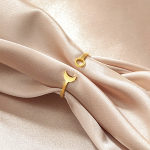 Detail of gold open ring with moon and sun charms on champagne satin fabric texture