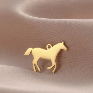Détail du pendentif cheval en acier doré 18 carats sur un tissu en soie champagne