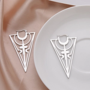 Detailed view of silver stainless steel hollow cross and triangle earrings on silk fabric