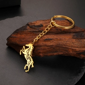 Golden stainless steel keychain with hollow Celtic horse pendant on dark wood background