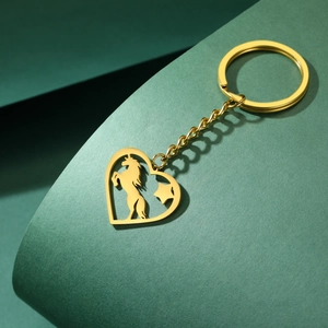 Détail d'un porte-clés cœur doré en acier inoxydable avec silhouette de cheval sur vert