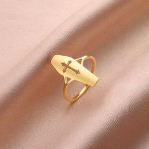 Anillo de ataúd dorado con diseño de cruz hueca sobre un fondo de tela de seda