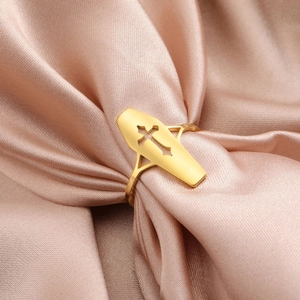 Detalle del anillo de cruz en acero dorado sobre un elegante tejido de seda color champán