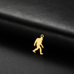 Golden Bigfoot silhouette pendant in polished stainless steel on a black leather background